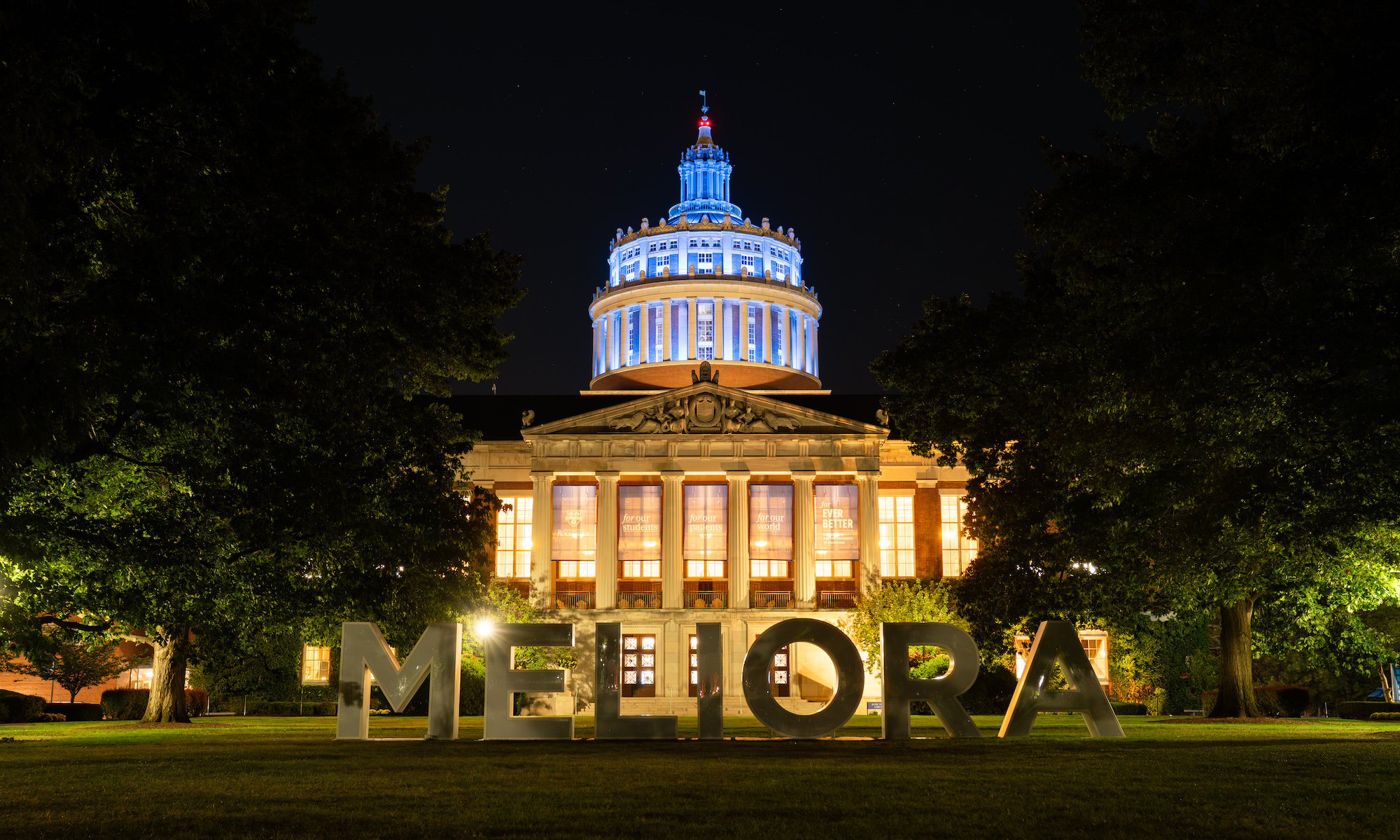 Rush Rhees Library and the Meliora sign illuminated at night.