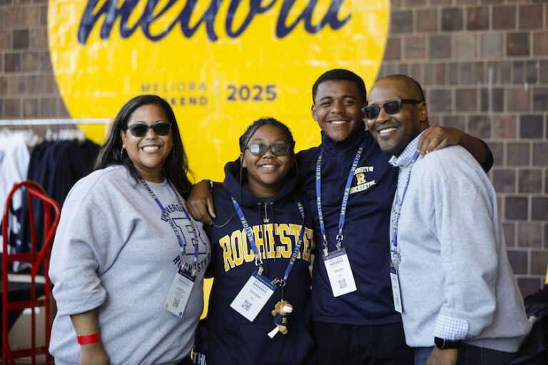 A group of four people in Rochester sweatshirts pose happily for a photo.
