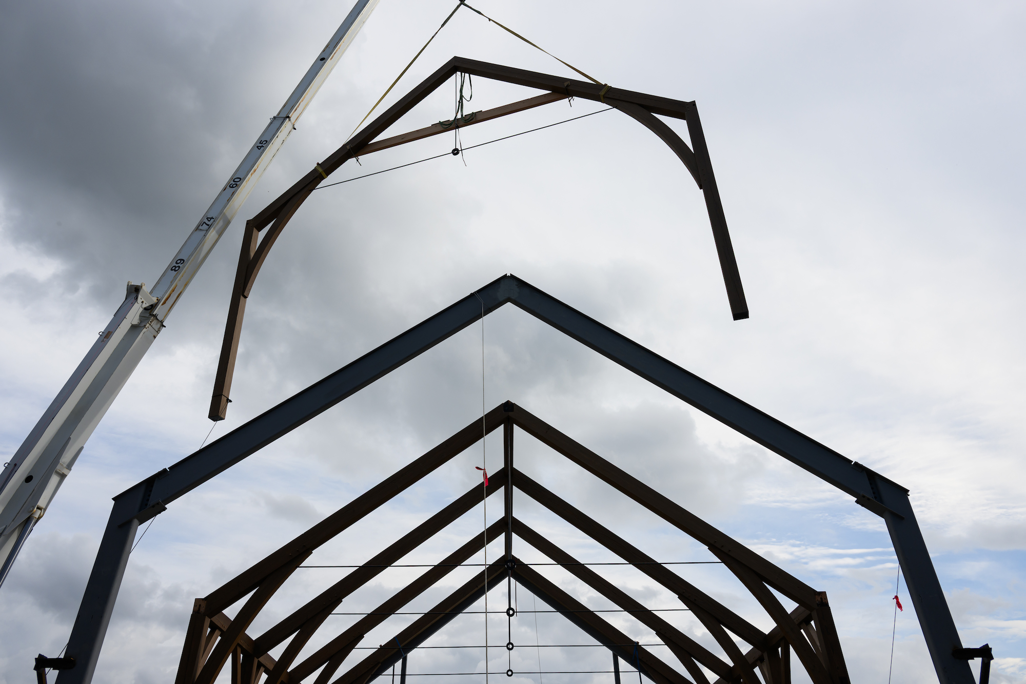 A crane lowers the last timber frame truss on a construction project. 