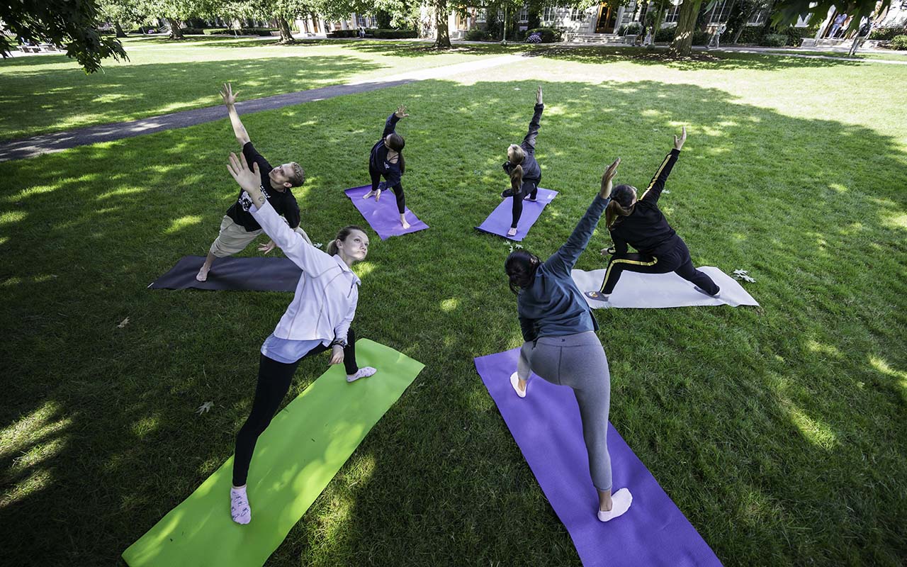 Six University of Rochester students do yoga outside on the quad to manage stress and build resilience.