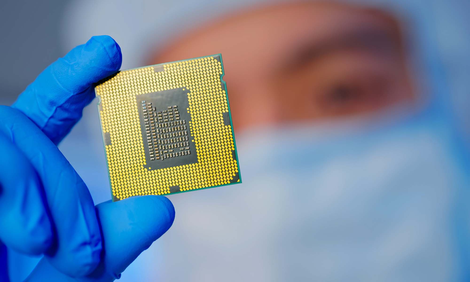Close up of a semiconductor microchip held by an Asian male engineer in sterile coveralls and gloves.