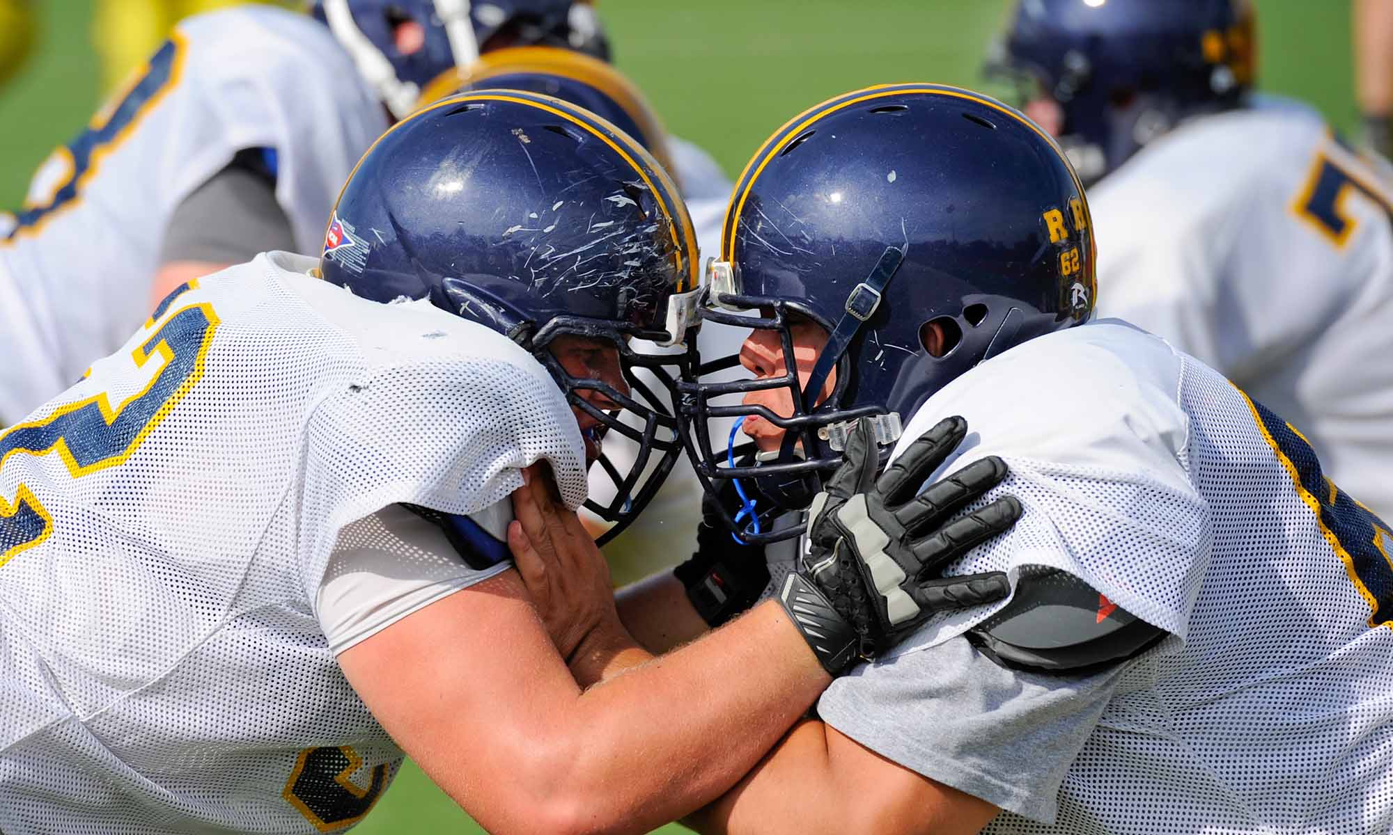 Close up of two football players running a contact drill to illustrate how concussions and head injuries can occur during sports.