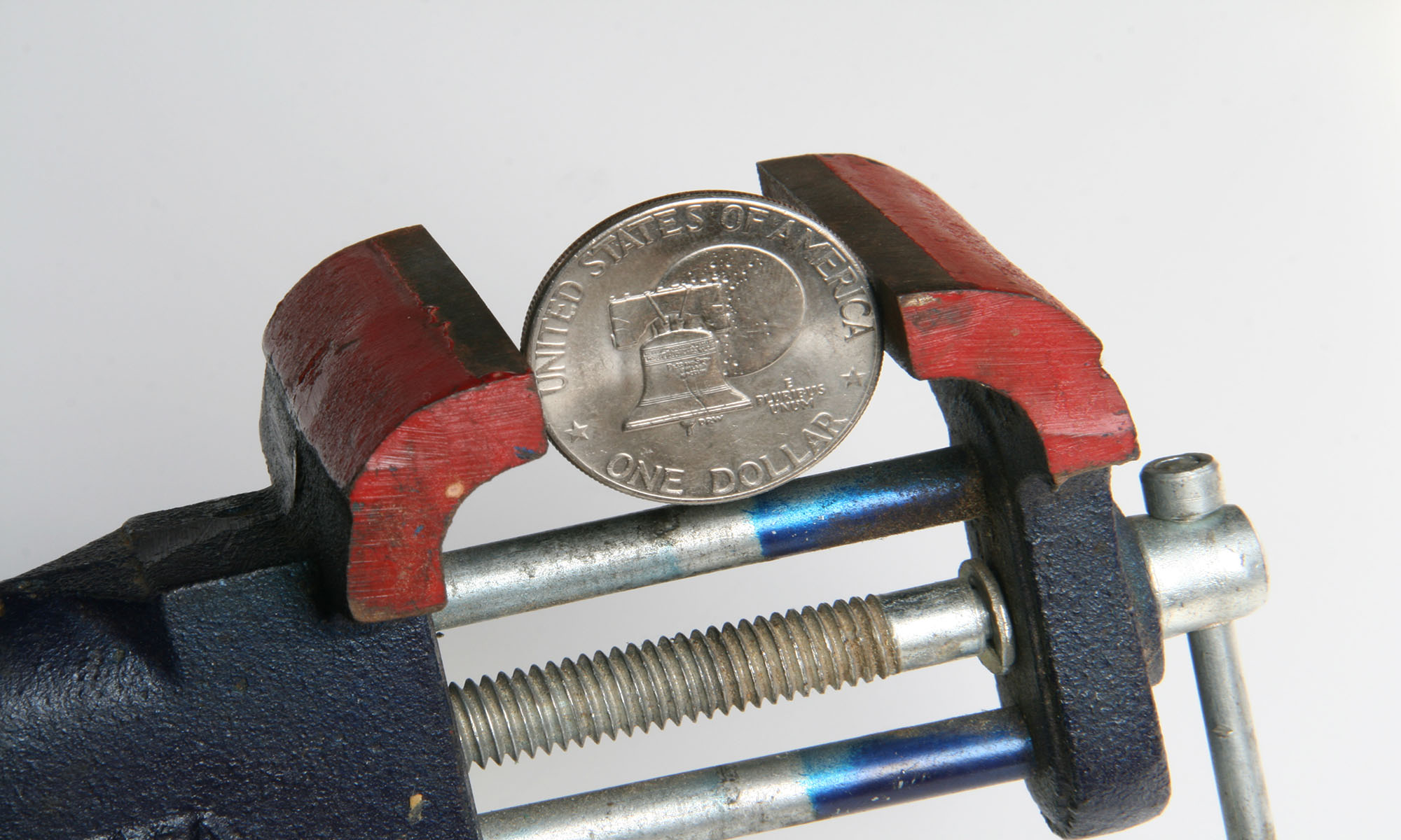 A vise tool holding a coin that says United States of America one dollar.