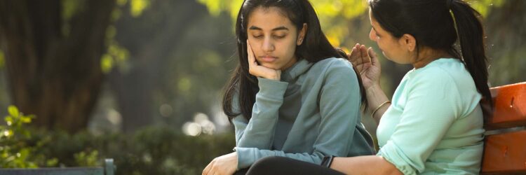 A mother comforts her daughter on a park bench.