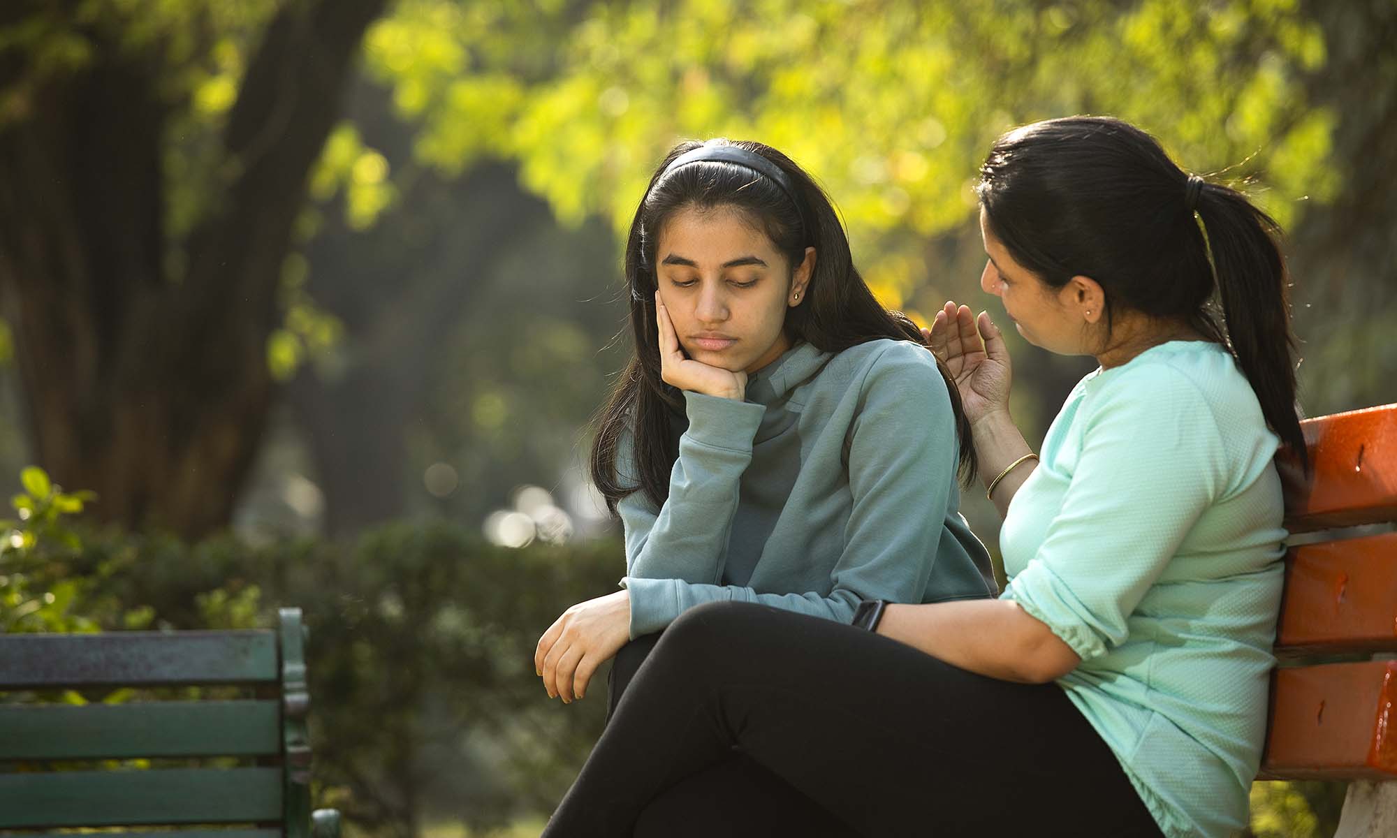 A mother comforts her daughter on a park bench.