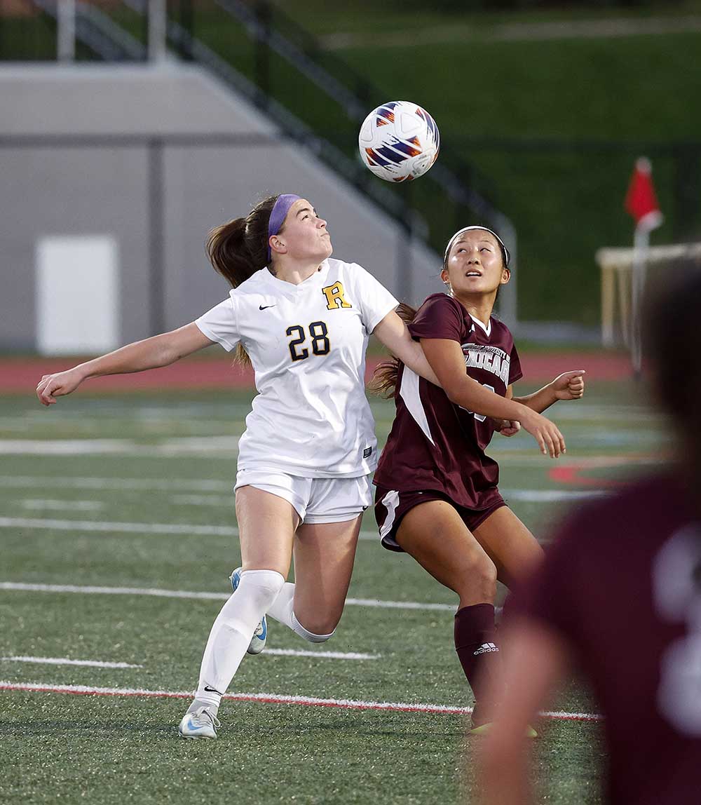 University of Rochester women's soccer play heading a ball with a rival team member nearby.