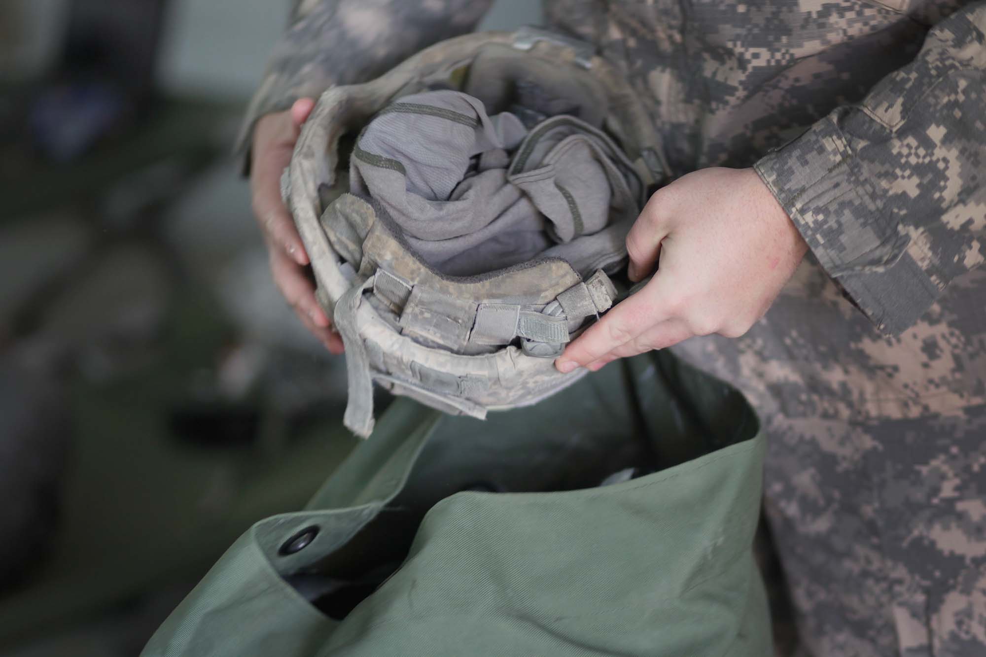 US army soldier's hands hold a helmet near an open rucksack. 