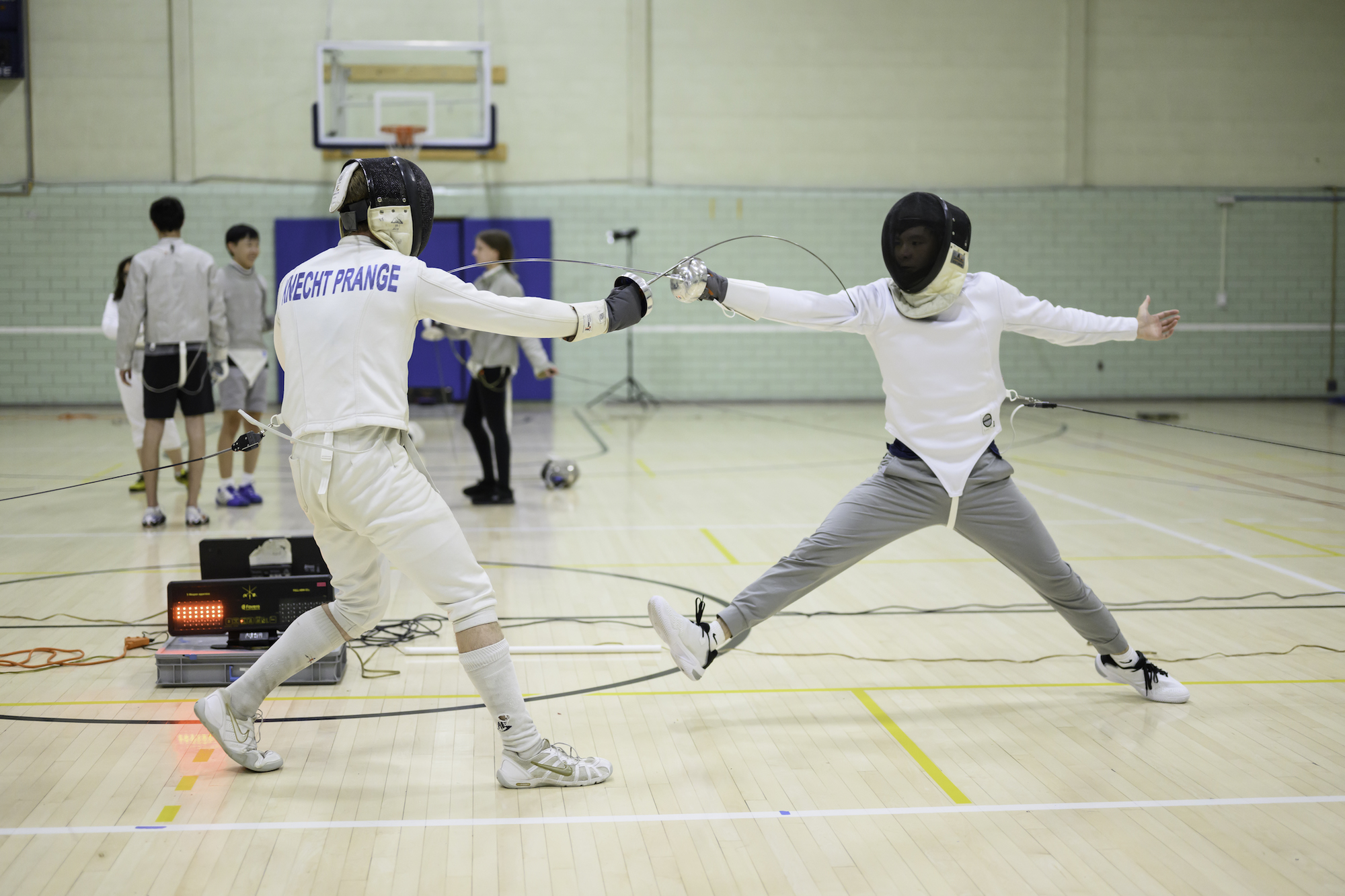 Two students in gear spar during a fencing club practice.