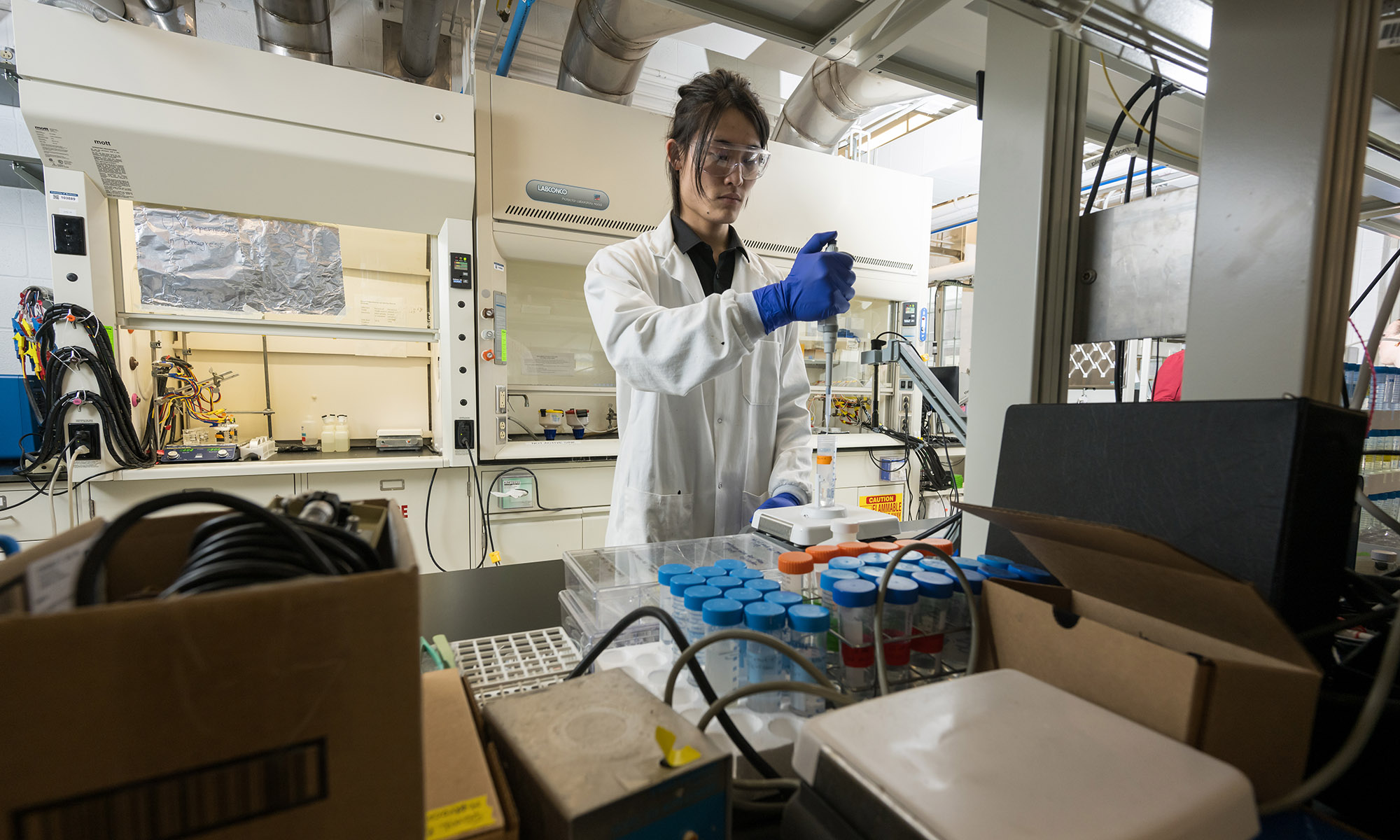 Researcher in a lab coat and gloves uses a pipette with test tubes.