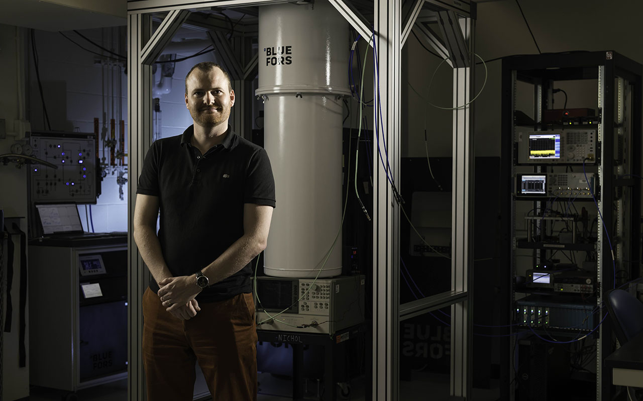 Machiel Blok, whose research builds on the fundamentals of quantum tunneling, in front of a BlueFors dilution refrigerator smiles and looks at the camera.
