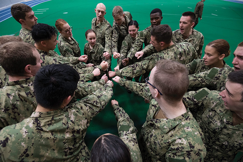 A group of soldiers standing in a circle, joining hands in unity, symbolizing teamwork and camaraderie.