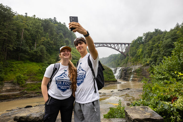 Two members of UR Foot take a selfie in front of the bridge in Letchworth Park.