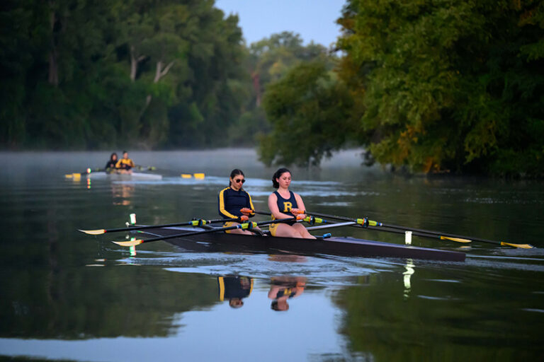 Two boats with two crew team members each rowing on the Genesee River.