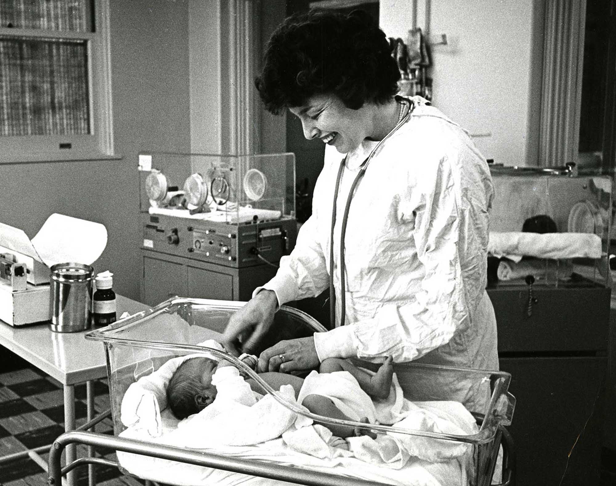 Black and white archival photo of Ruth Lawrence as a young physician checking a newborn baby in a hospital crib.