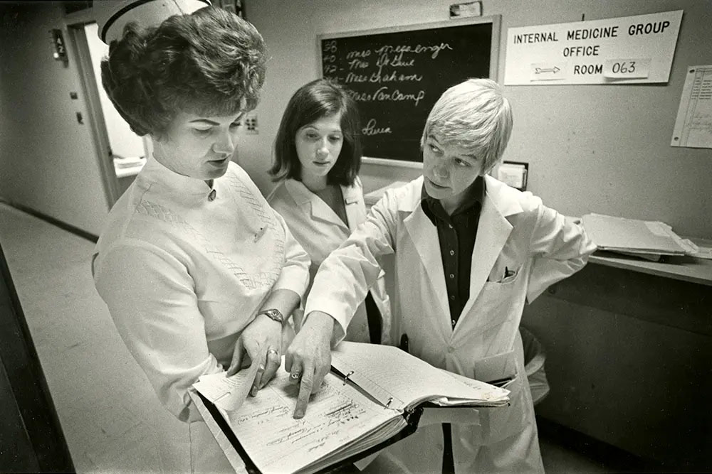 Three women in lab coats examining a document together in a laboratory setting.