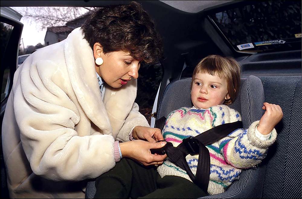 A woman assists a child in a car seat, ensuring their safety and comfort while preparing for a journey.