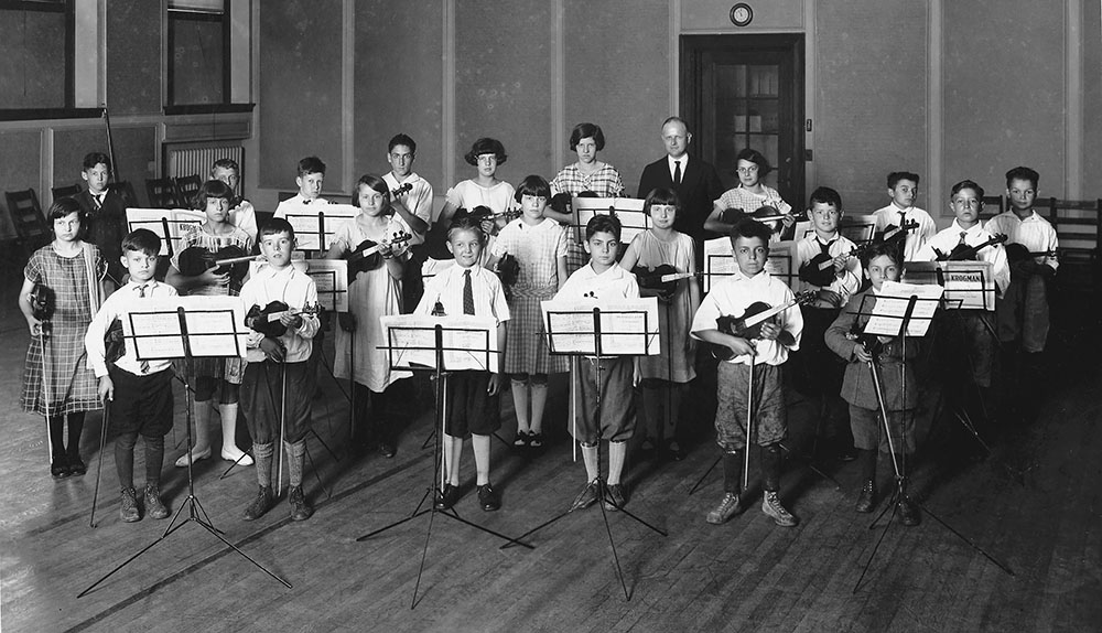 A group of children gathered in a room, focused on music stands while practicing their instruments.