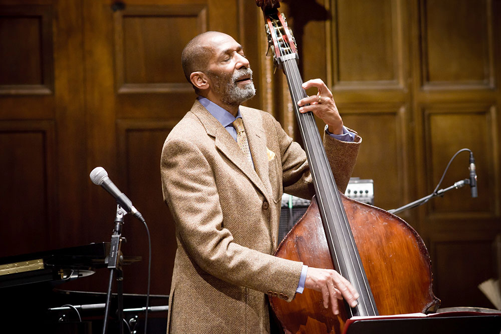 A man in a suit, Ron Carter, skillfully playing a double bass on stage.