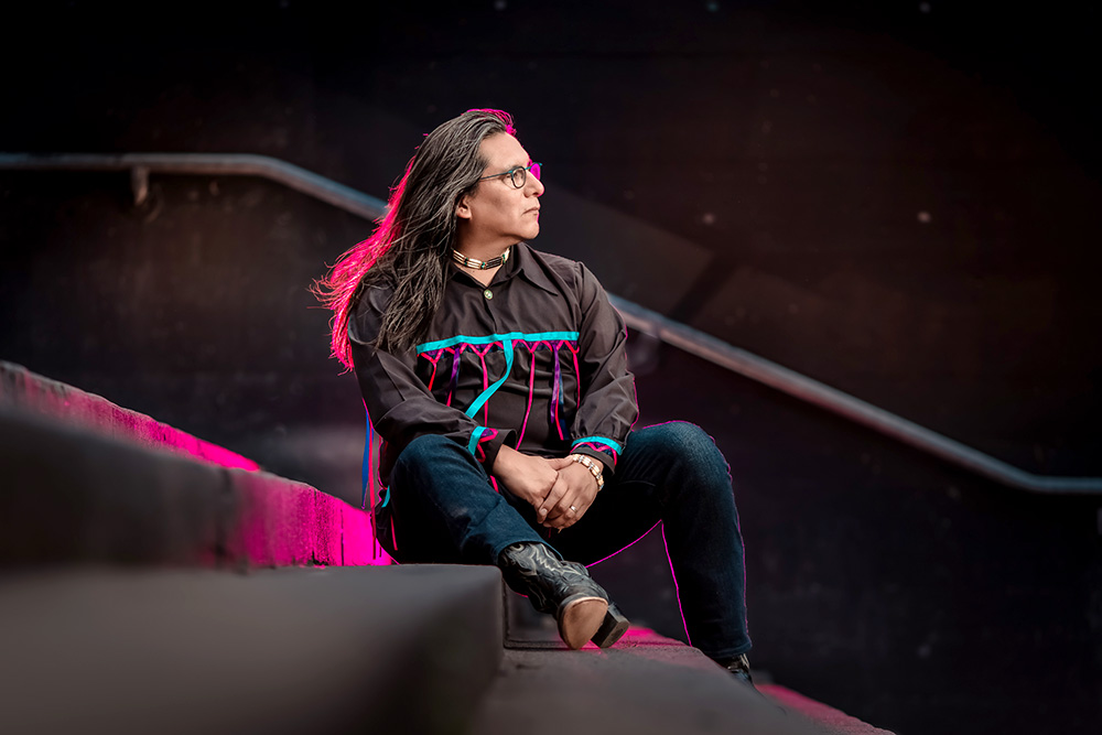 A man in a traditional Native American outfit sits on a stairway, showcasing his cultural attire and surroundings.