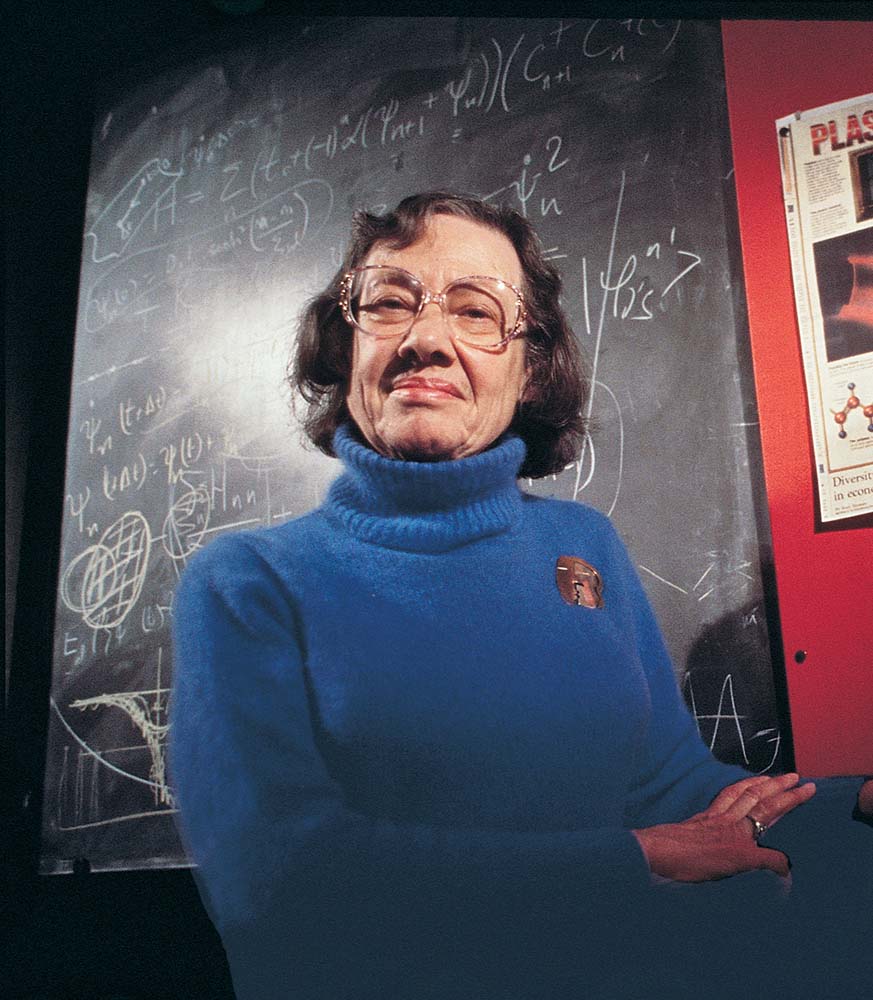 Esther Conwell, in a blue sweater, seated before a blackboard, likely teaching or presenting information.