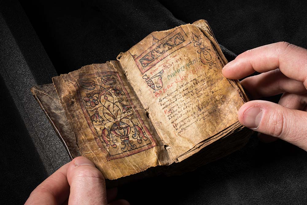 A person holding an old book with handwritten text on its pages, showcasing its vintage appearance and historical significance.