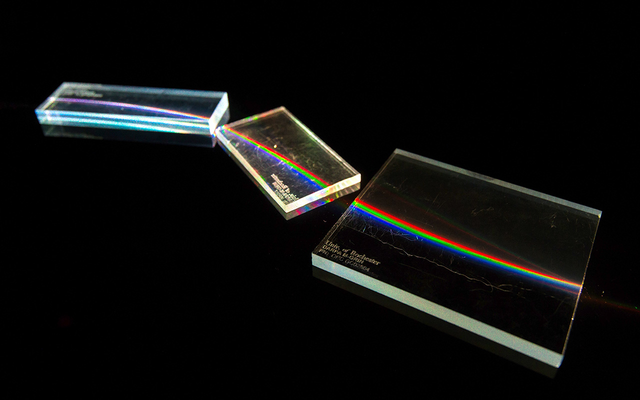 Three gradient-index lenses display rainbow-like light refraction, illustrating advanced optical design developed at URochester.