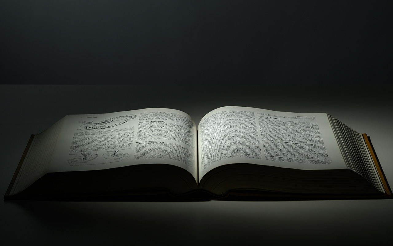 Schwartz's Principles of Surgery book lies on a dark surface, its pages illuminated to reveal dense text and scientific diagrams.