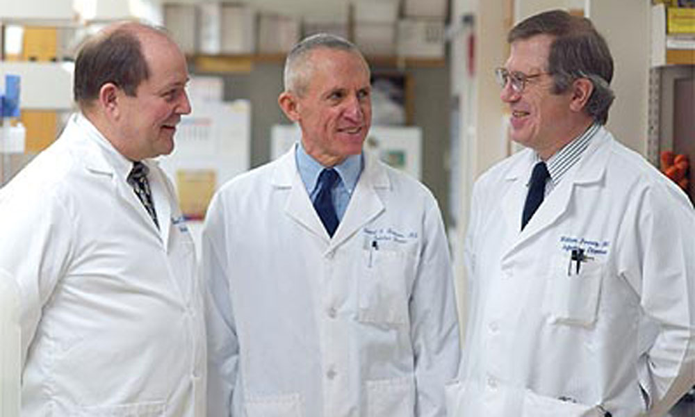 Three men in lab coats stand together at the University of Rochester, involved in HPV vaccine research.