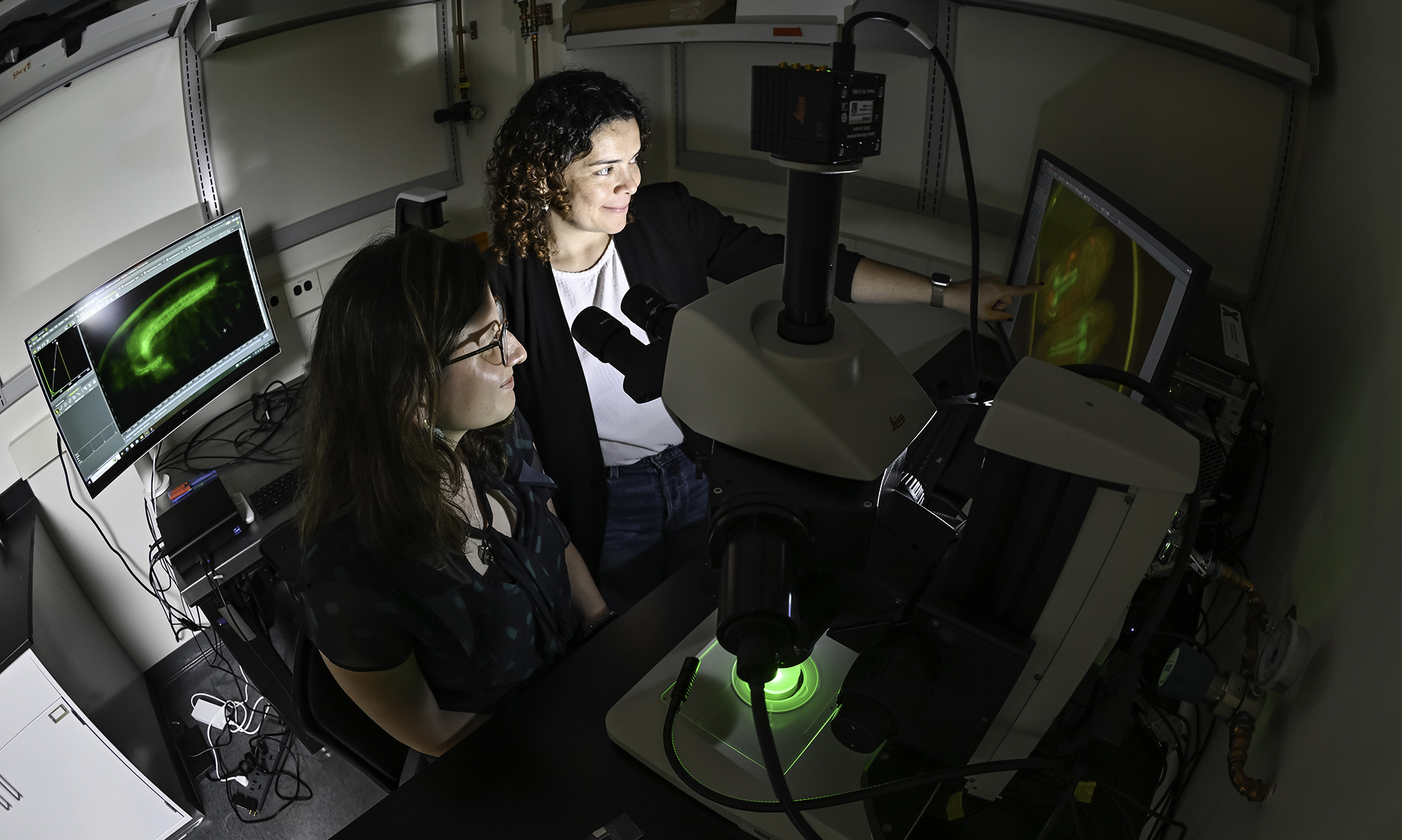 Marisol Herrera-Perez and Maria Camila Ferrucho leaning over a fluorescent microscope and several computer screens.
