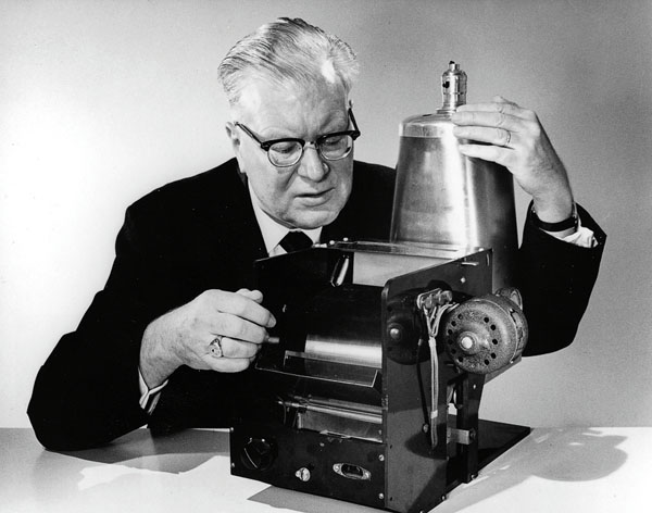 A man in glasses and a suit demonstrates a replica of the first xerographic machine at Carlson Library.