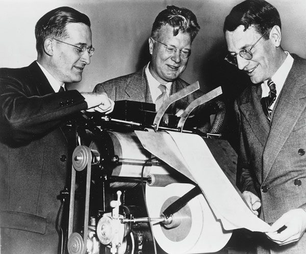 Three men in suits examine an experimental xerography machine at the Battelle Institute in 1948.