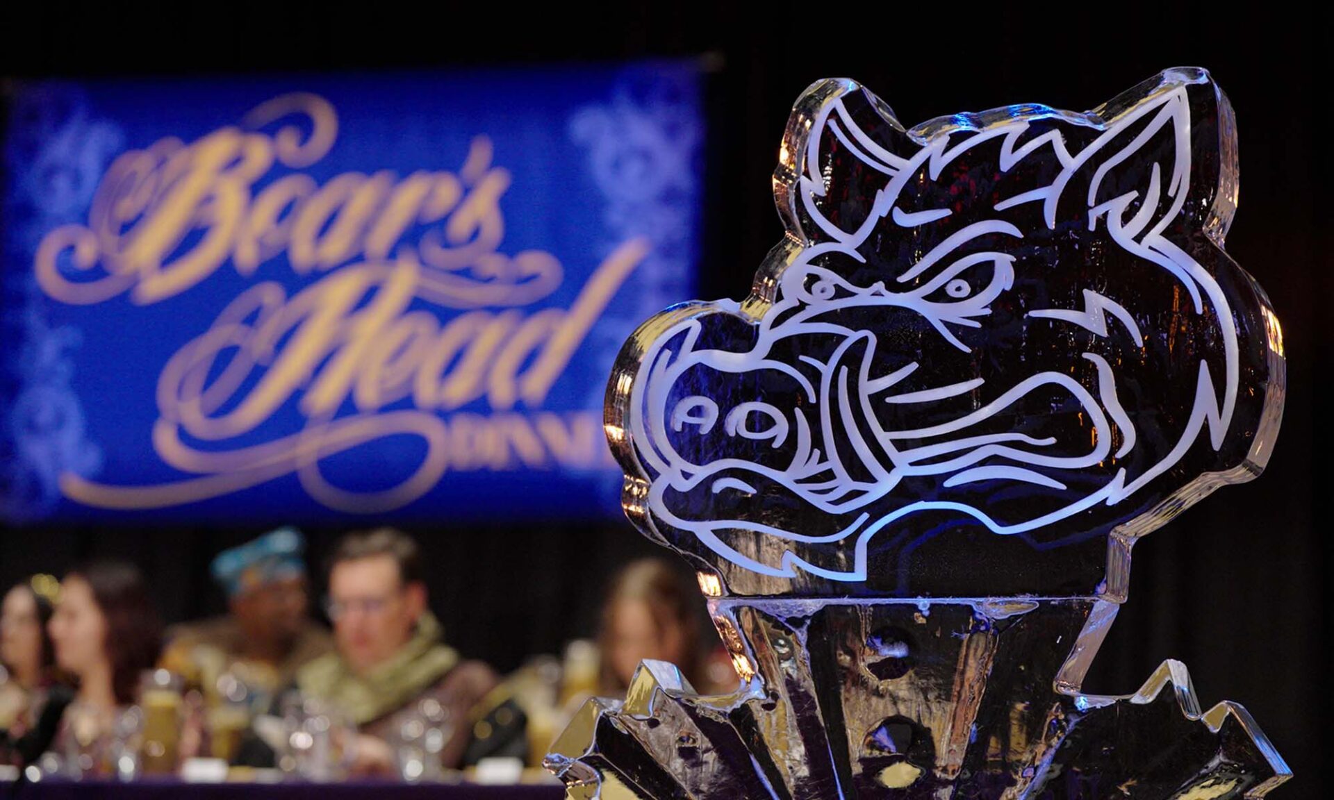 Close up of an ice sculpture of a boar's head with a screen in the background that reads