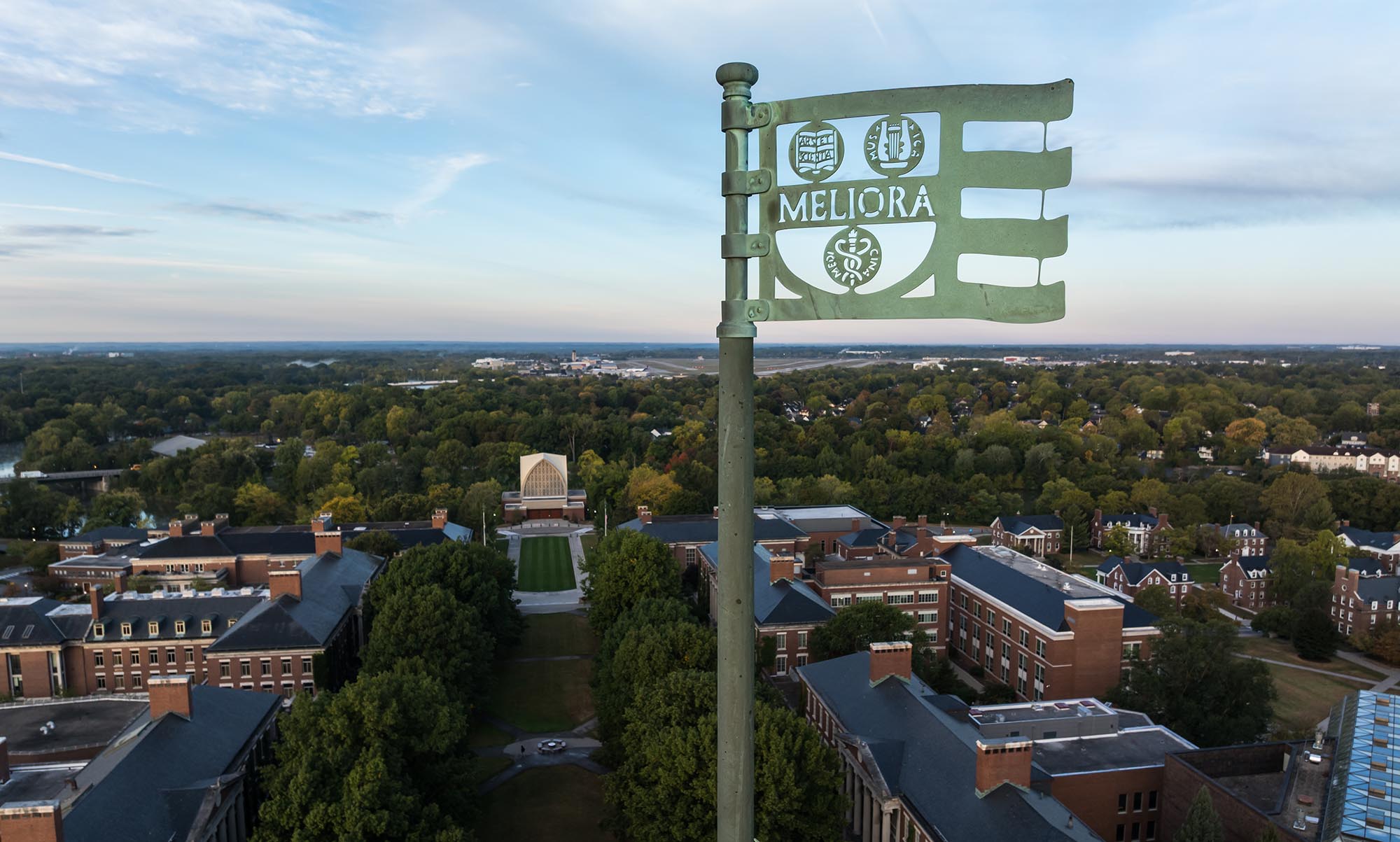 Aerial view of the University of Rochester campus with the Meliora flag and Rush Rhees Library tower at sunrise.