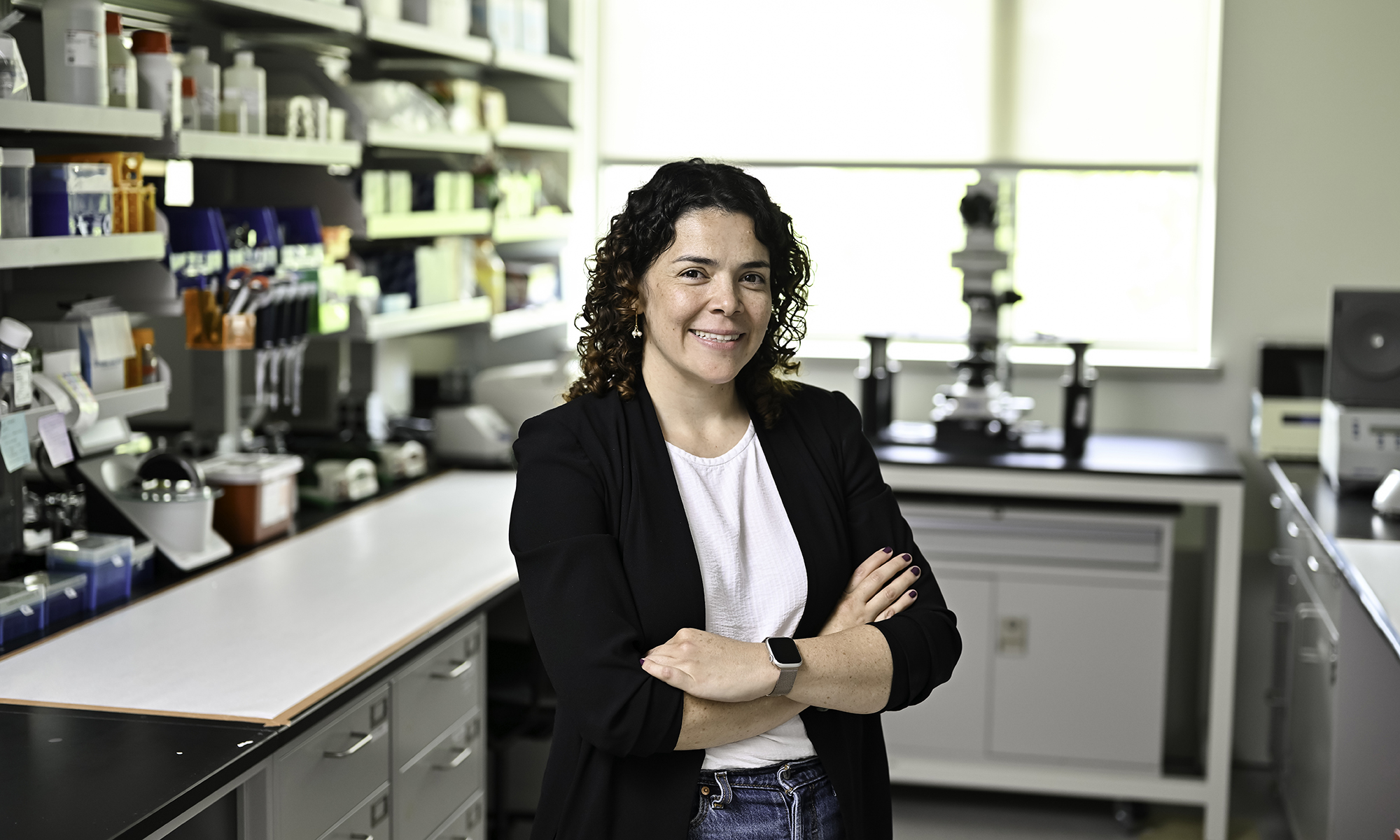 Marisol Herrera-Perez standing with her arms crossed next to a shelf of lab equipment.