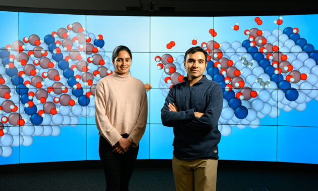 Siddharth Deshpande and Snehitha Srirangam standing in front of a large screen showing molecule simulations.