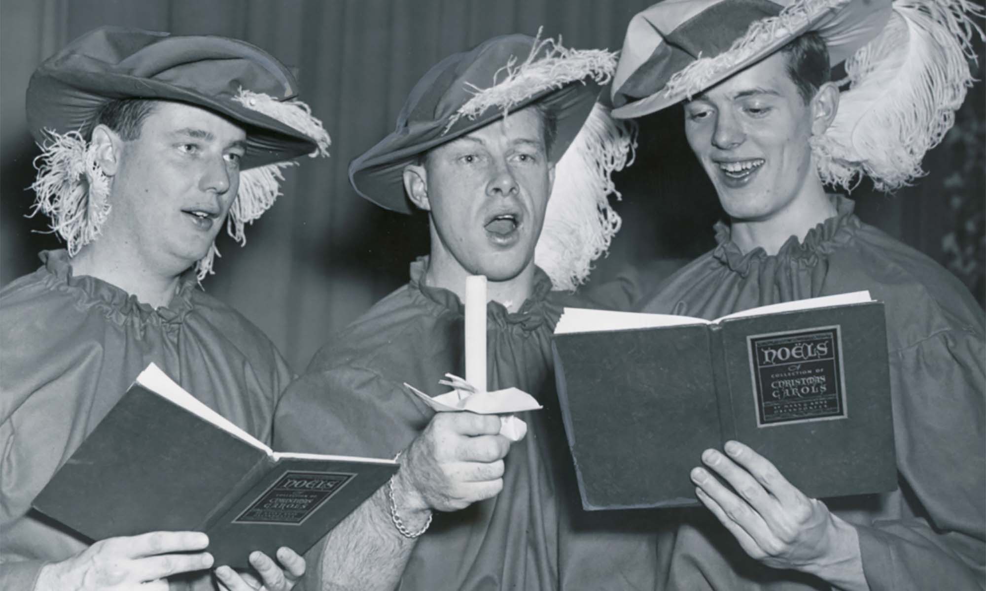 Black and white archival image of three University of Rochester undergraduates in medieval garb singing songs from a songbook.