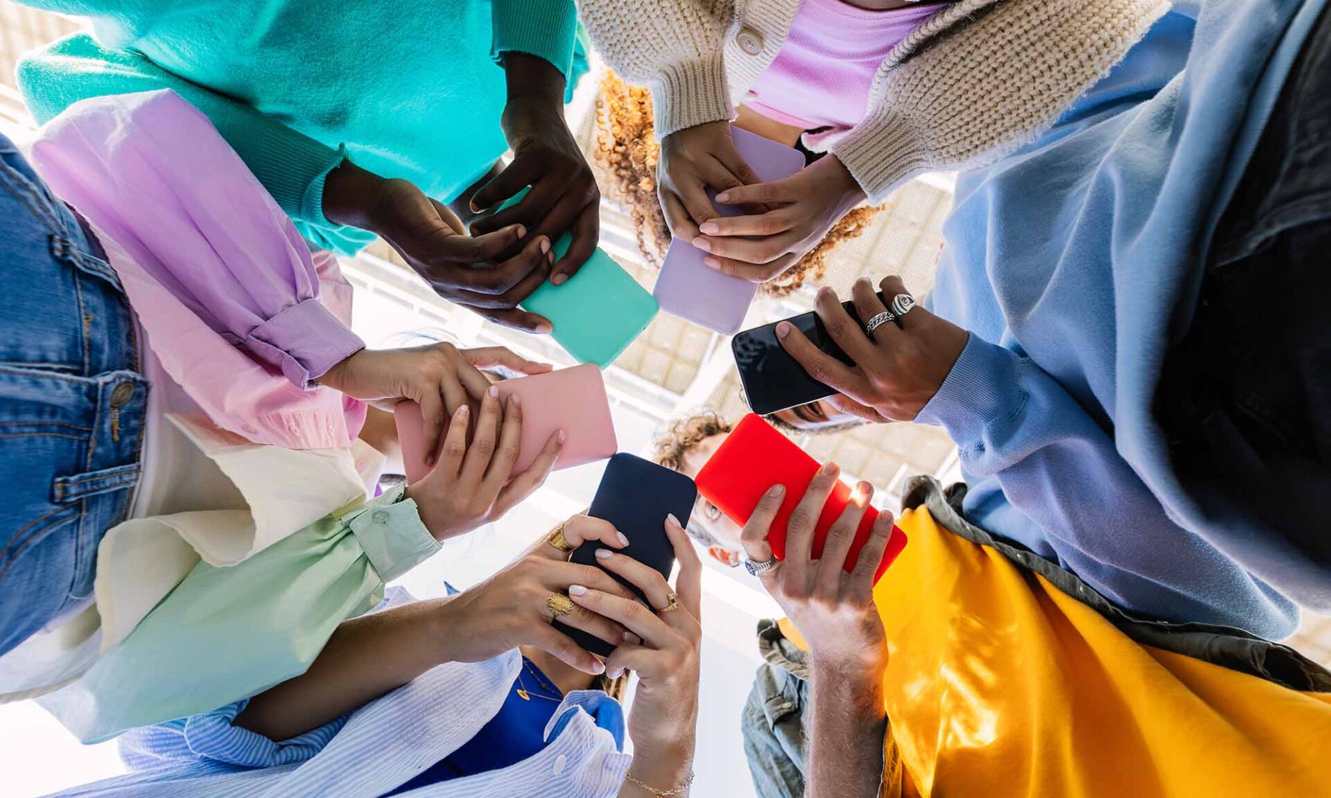 Low angle view of a young group of people in a circle holding cellphones to illustrate crowdsourced fact-checking on social media, including Community Notes on X.