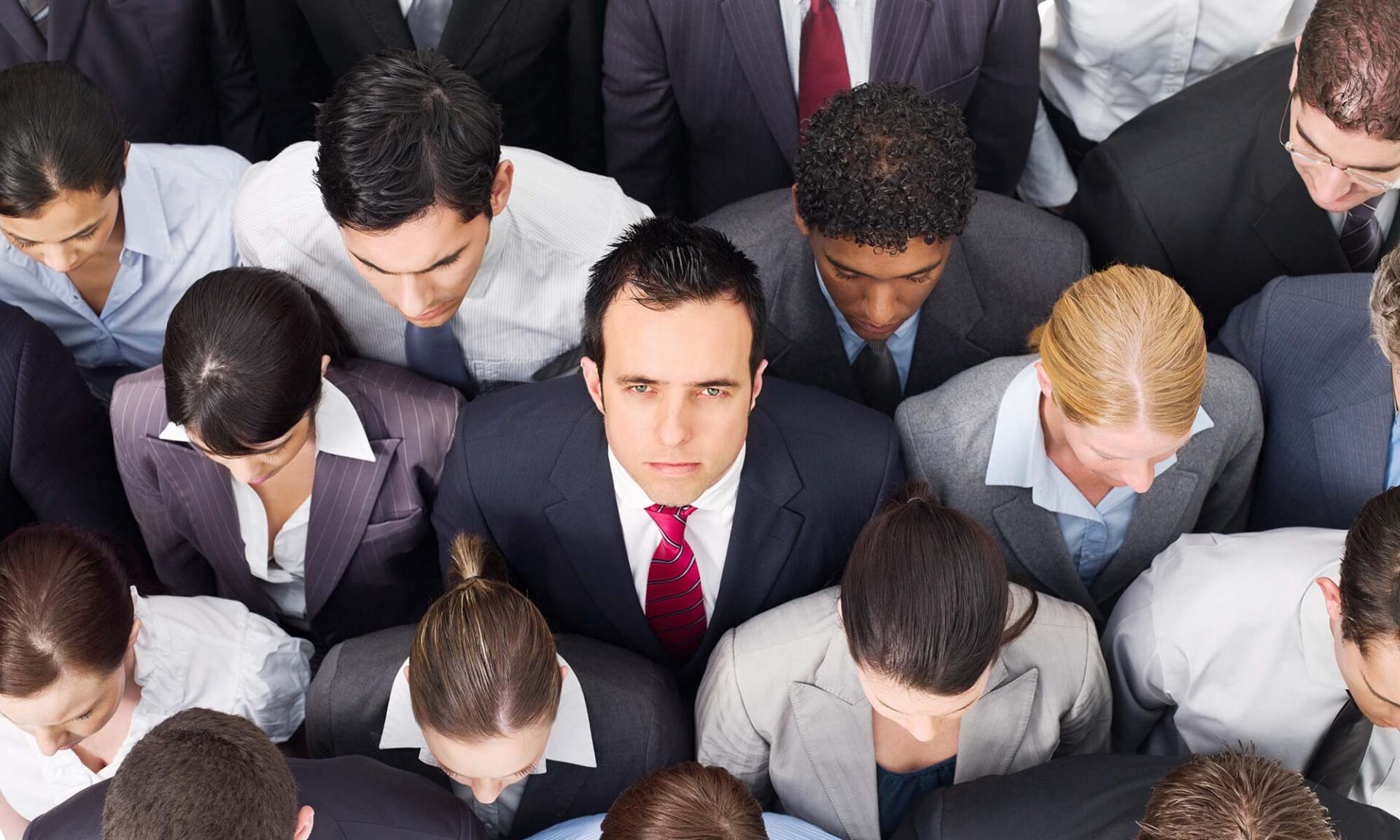 Overhead view of young business professionals tightly grouped and staring ahead, except for one man looking up in dismay to illustrate employee turnover at top firms.