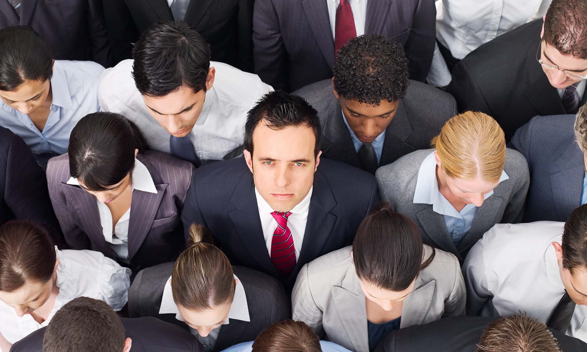Overhead view of young business professionals tightly grouped and staring ahead, except for one man looking up in dismay to illustrate employee turnover at top firms.