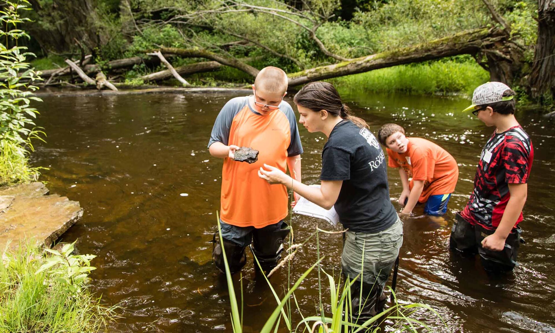 A teacher and three students wade in a creek as part of the curriculum at their rural schools in New York State.
