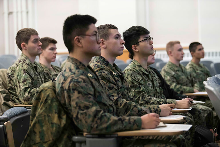 URochester NROTC midshipmen in uniform seated in a classroom.