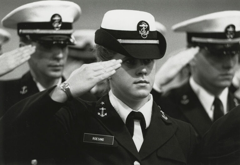 Close up of a black and white archival photo of NROTC cadets in uniform and saluting.