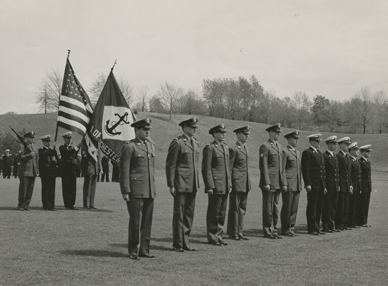 Black and white archival photo of University of Rochester NROTC cadets in uniform and standing at attention outdoors on campus.