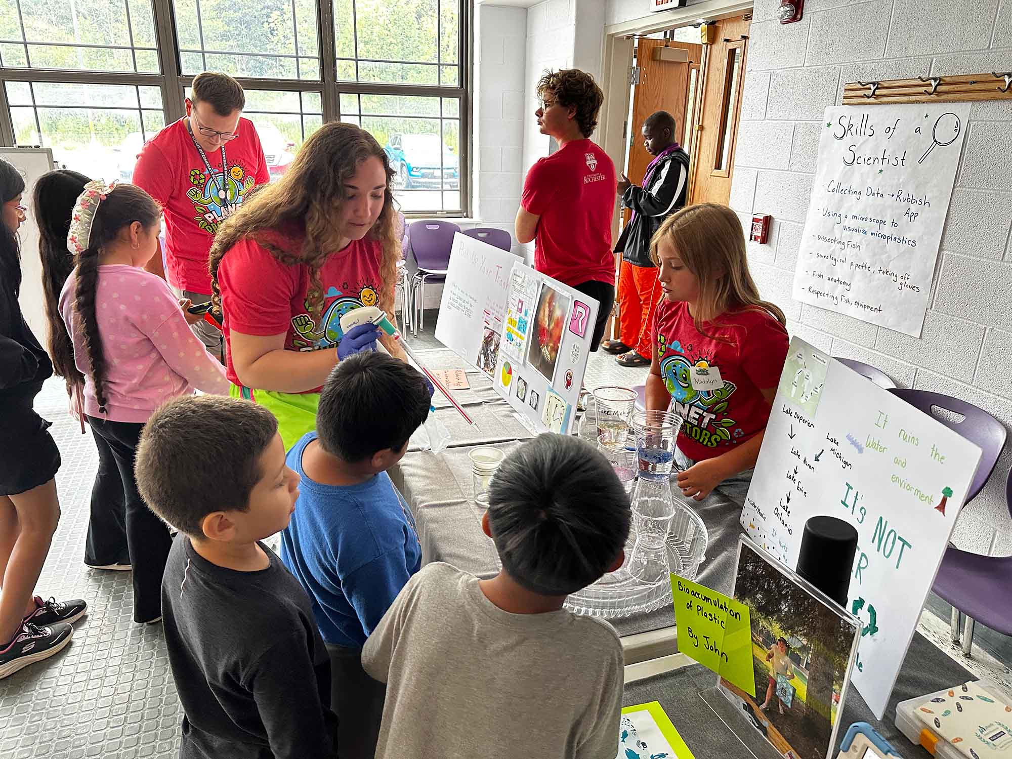 Educator-in-training Claire Tuttle speaks with several Sodus rural school children near a table with pamphlets and posters.