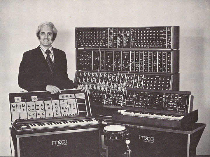 Black and white archival photo of Robert Moog next to a Moog synthesizer in the 1970s.