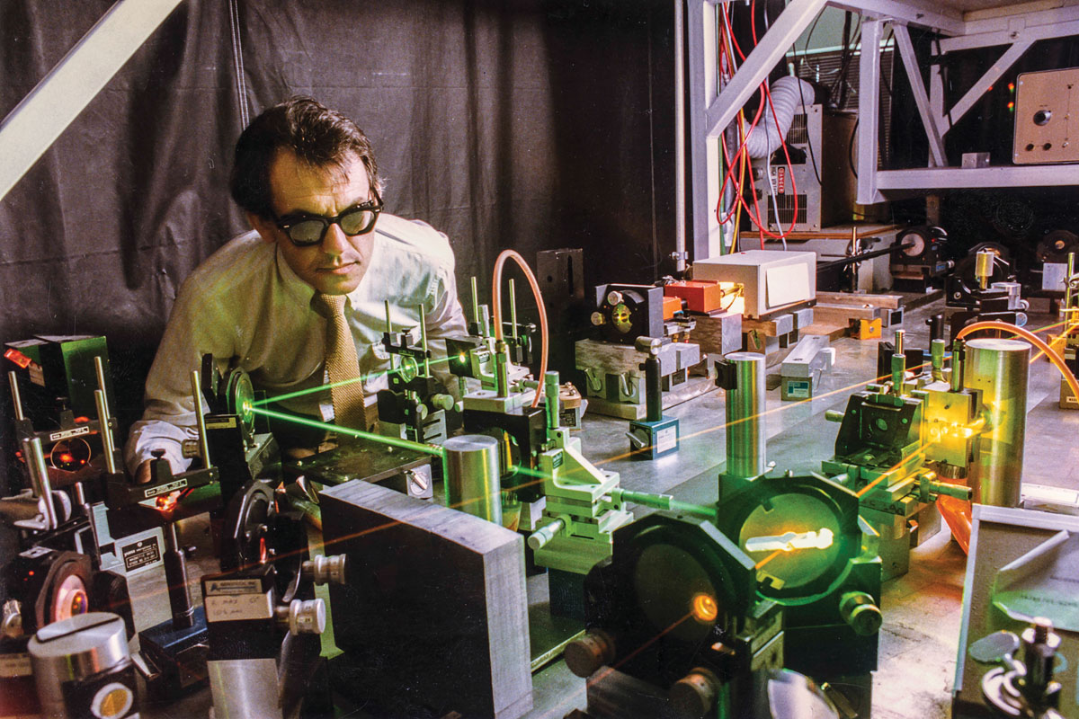 A man wearing glasses and a tie operates a machine, focused on his work in a professional setting.