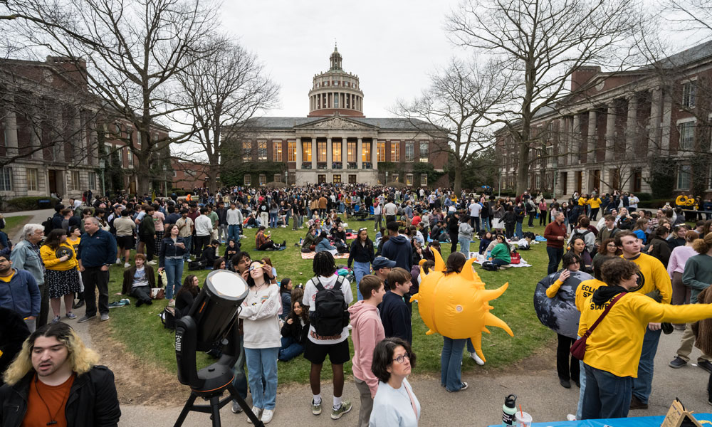 A crowd of University of Rochester students gathered outside a building for an eclipse watch party.