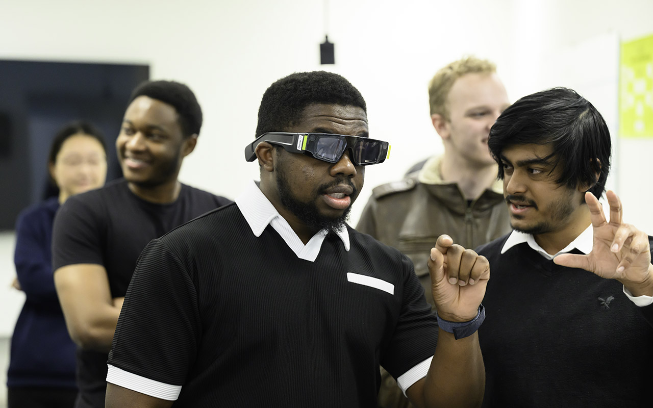 Students test AR/VR smart glasses in a classroom, with one gesturing while others watch and discuss the experience.