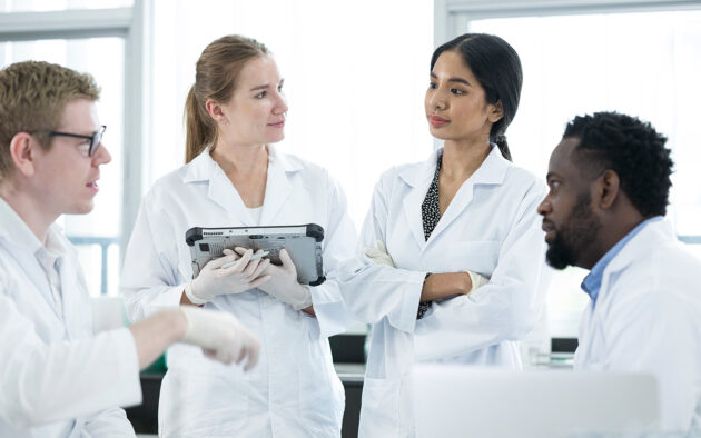 Diversity of scientists or researchers discussing their research result data in a laboratory and wearing typical white lab coat.
