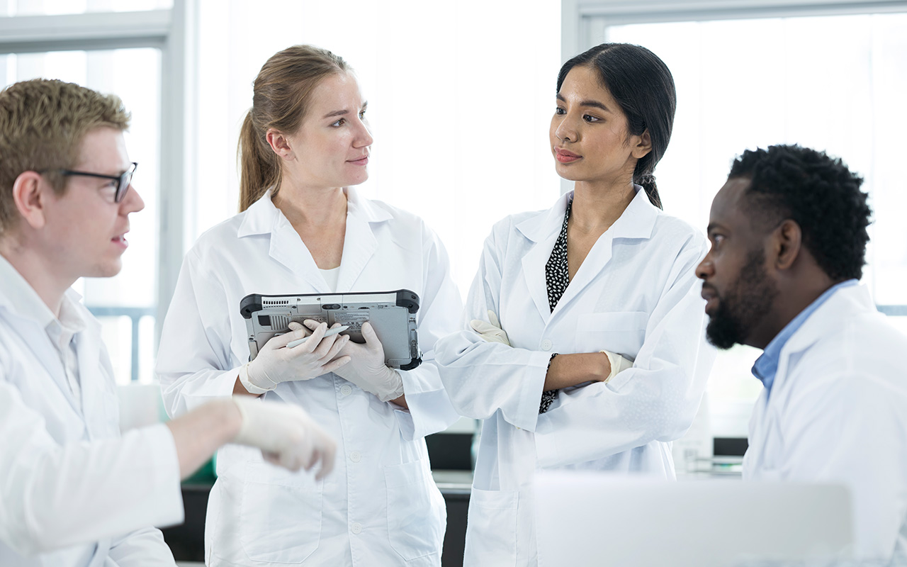 Diversity of scientists or researchers discussing their research result data in a laboratory and wearing typical white lab coat.